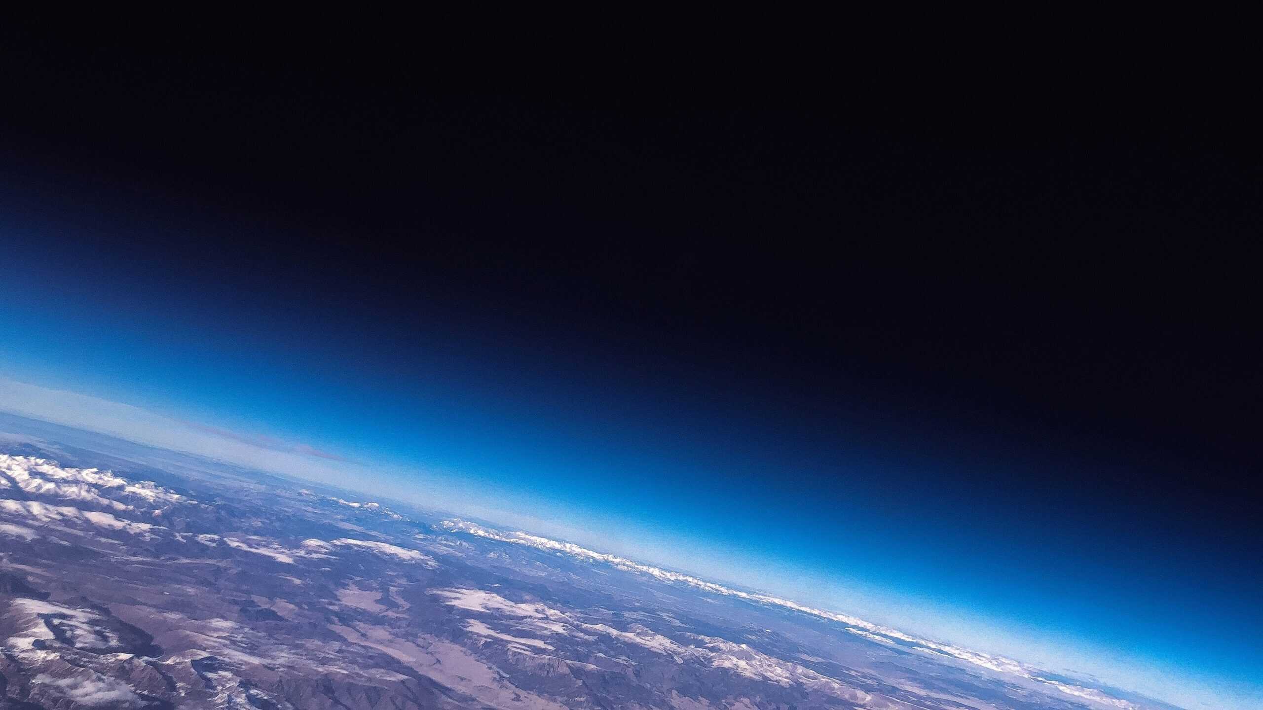 Vivid view of Earth's atmosphere and horizon from high-altitude, showcasing the blue sky transition and snowy mountains below.