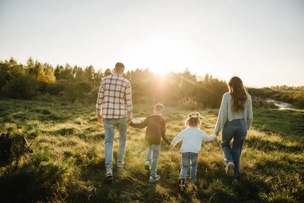 Family walking outdoors at sunset in a green field, enjoying nature and quality time together.